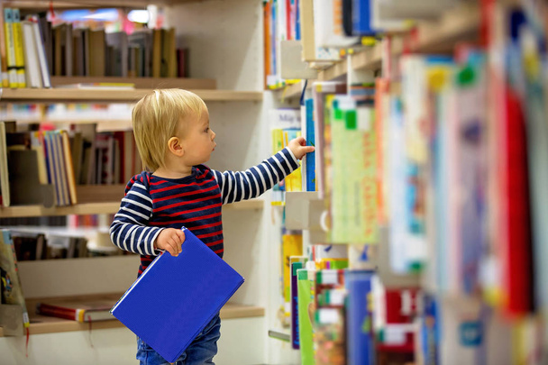 Smart todller boy, educating himself in a library, reading books - Zdjęcie, obraz