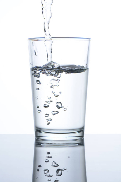 Pouring water into a glass on white background - Photo, Image