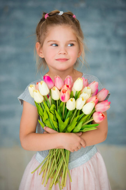 Adorable smiling little girl with tulips by the window - Foto, afbeelding