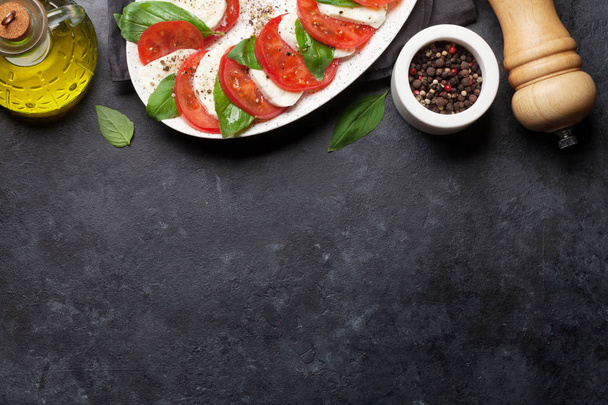 Traditionele Italiaanse Caprese salade met rijpe tomaten, verse tuin basilicum en mozzarella kaas op steen achtergrond - Foto, afbeelding