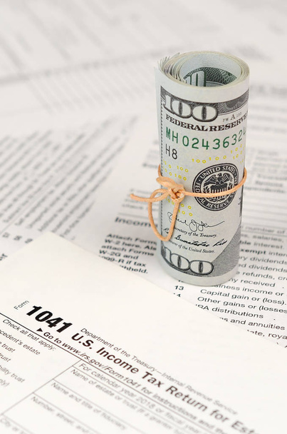 1041 US Income tax return for Estates and Trusts form with roll of american dollar banknotes close up. Концепция налогового периода в США
 - Фото, изображение