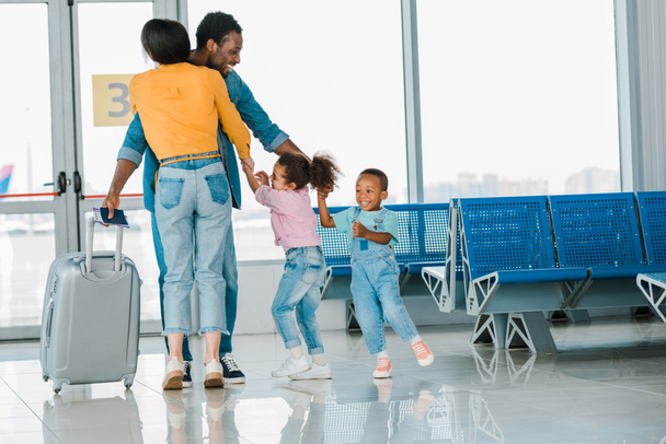 счастливый африканский американец обнимает детей и жену в аэропорту
 - Фото, изображение