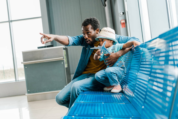african american father pointing with finger away while son holding toy plane in airport  - Foto, Bild