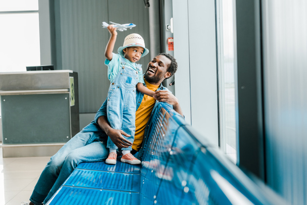 happy african american father looking at son while boy playing with toy plane in airport - 写真・画像