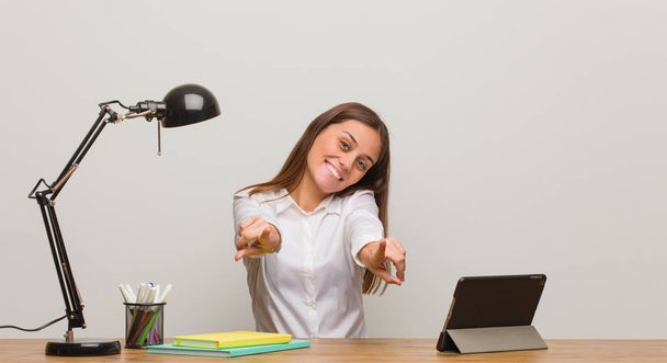Молодая студентка, работающая за своим столом весело и улыбаясь указывая на фронт
 - Фото, изображение