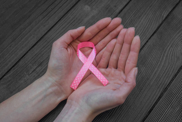  Dames handen houden roze lint op zwarte houten achtergrond, borstkanker Awareness maand, concept van de gezondheid.  - Foto, afbeelding