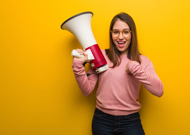 Young cute woman holding a megaphone surprised, feels successful and prosperous - Photo, Image
