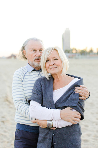 Ανώτερος σύζυγος αγκαλιάζει Καυκάσιος σύζυγος σε άμμο φόντο παραλία. - Φωτογραφία, εικόνα