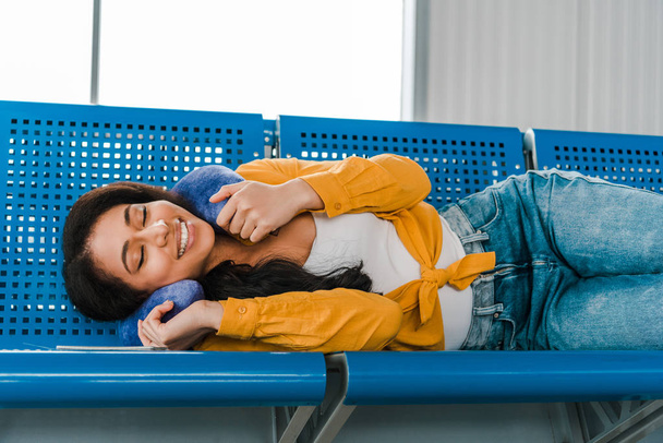 усміхнена афроамериканка лежить на сидіннях з подушкою для подорожей і закритими очима в залі для відправлення
 - Фото, зображення