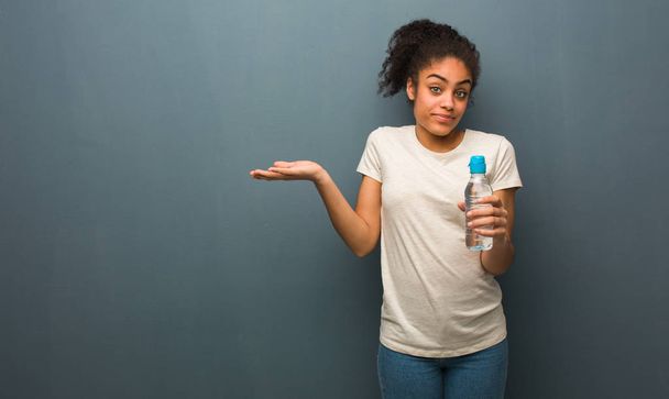 Genç siyah kadın şüpheden ve omuz Shrugging. O bir su şişesi tutuyor. - Fotoğraf, Görsel