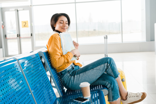 空港の出発ラウンジで地図を保持している間に目を閉じていくためにコーヒーと座っている喜ぶアフリカ系アメリカ人の女性 - 写真・画像