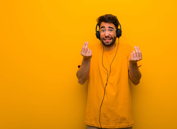 Young man listening to music doing a gesture of need - Foto, afbeelding
