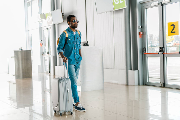 handsome african american man walking with suitcase in airport - Fotó, kép