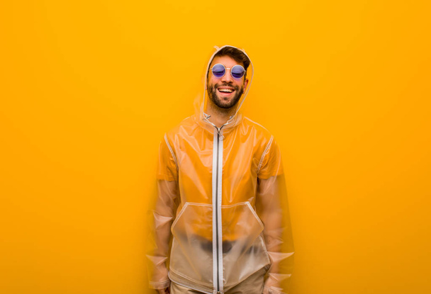 Giovane uomo che indossa un cappotto antipioggia allegro con un grande sorriso
 - Foto, immagini