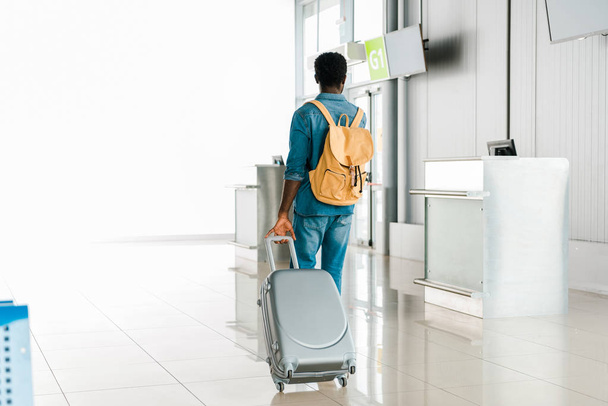 vista trasera del hombre afroamericano caminando con equipaje y mochila en el aeropuerto
 - Foto, imagen
