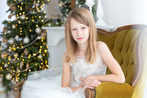 Girl sitting in the armchair next to Christmas tree - Fotoğraf, Görsel