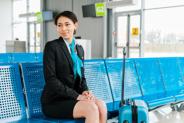 attractive african american stewardess sitting with suitcase in departure lounge - Photo, Image