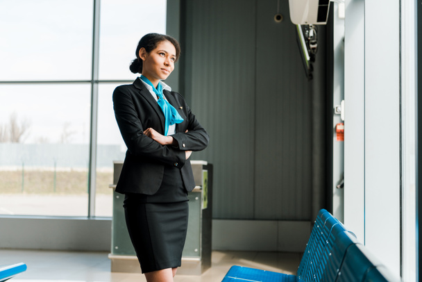 african american stewardess standing with crossed arms in airport and looking at window - Photo, Image