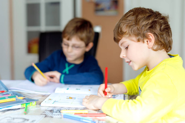 Dos niños pequeños en casa haciendo deberes. Pequeños niños concentrados escribiendo con lápices de colores, en el interior. Escuela primaria y educación. Hermanos y mejores amigos aprendiendo
. - Foto, imagen