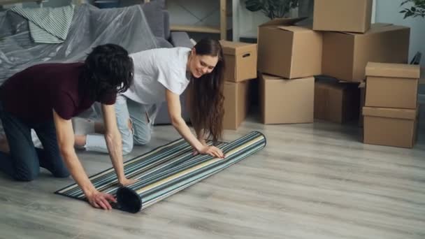 一緒に新しいアパートに引っ越した後、床にカーペットを転がす男性と女性 - 映像、動画