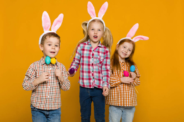 two little girls and boy with Easter bunny ears holding colorful eggs - Fotoğraf, Görsel