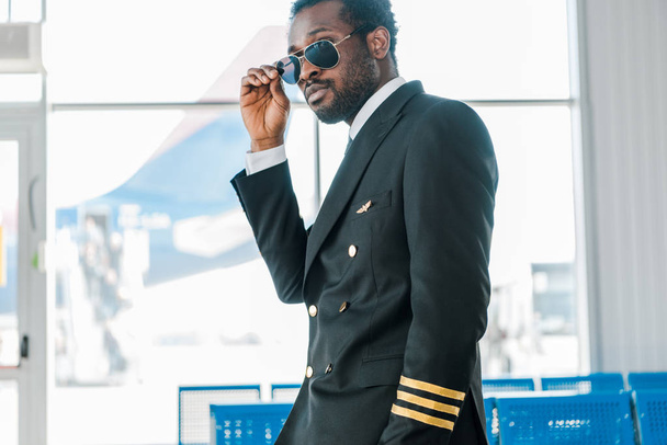 stylish confident african american pilot in sunglasses in departure lounge in airport - Foto, afbeelding