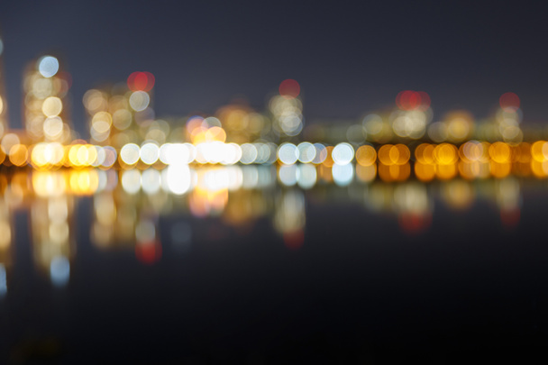 blurred dark cityscape with illuminated buildings, reflection and bokeh lights - Foto, afbeelding