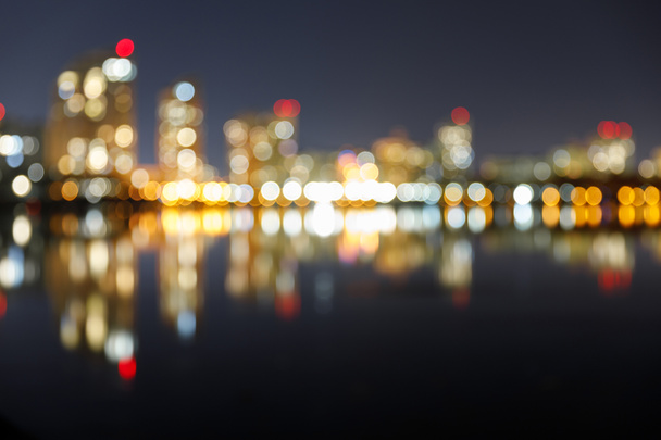 размытый темный городской пейзаж с освещенными зданиями, отражением и боке огни в ночное время
 - Фото, изображение