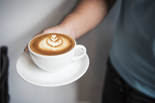 Hand vasthouden van Latte of cappuccino met schuimend schuim, koffie kopje  - Foto, afbeelding
