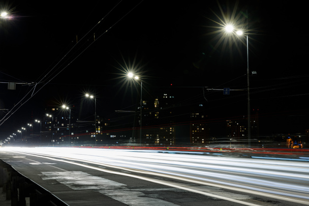 lange blootstelling van de lichten op de weg 's nachts in de buurt van gebouwen - Foto, afbeelding