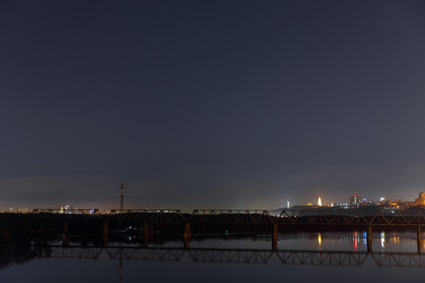 dark cityscape with calm river and bridge at night - Foto, afbeelding