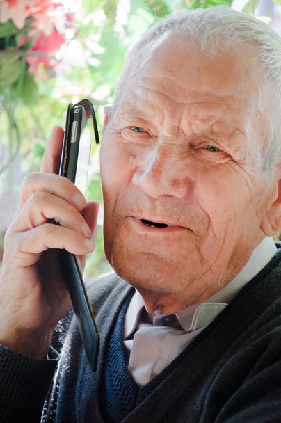 Starszy mężczyzna rozmawia przez telefon z córką. Dziadek komunikuje się ze swoją wnuczką lub poznaje radosną nowinę. Człowiek jest zadowolony, aby zadzwonić - Zdjęcie, obraz