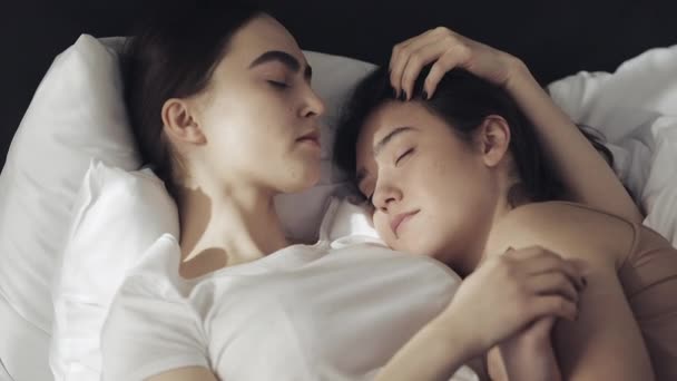 Lesbian couple embracing in the bed at home. One girl kisses another girl when she is sleeping Slow motion. Lifestyle, LGBT concept - Video