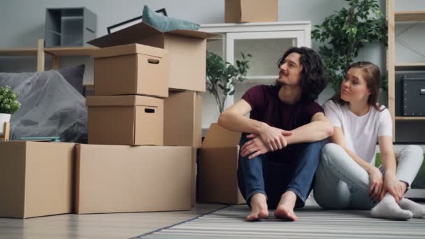 Mladá žena, která mluví s manželem a sedí na podlaze s krabic během přemístění - Záběry, video
