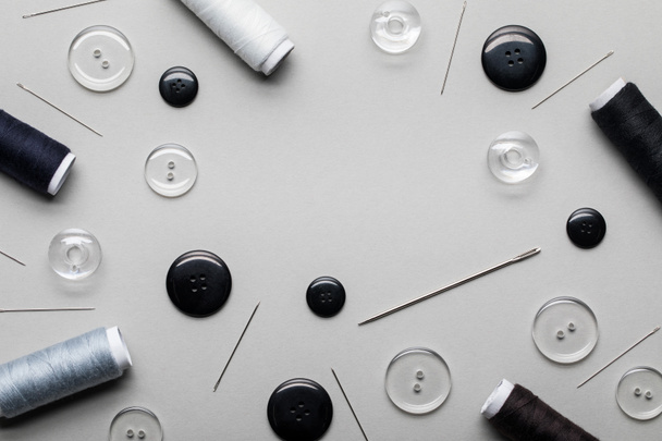 Ansicht von schwarzen und transparenten Kleidungsknöpfen, Nadeln und Fadenspulen isoliert auf grau - Foto, Bild