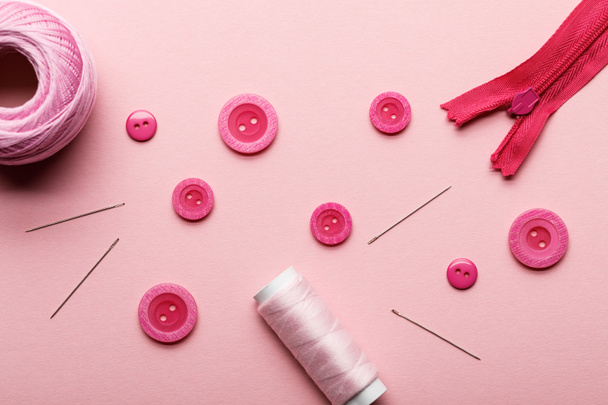 pohled na tlačítka oděvů, cívka s vlákny a šicí materiál izolované na růžovém - Fotografie, Obrázek