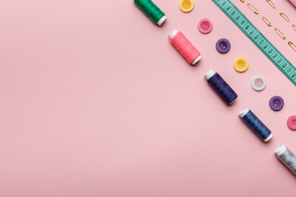 vista superior de bobinas de hilo de colores, botones y suministros de costura aislados en rosa con espacio de copia
 - Foto, imagen
