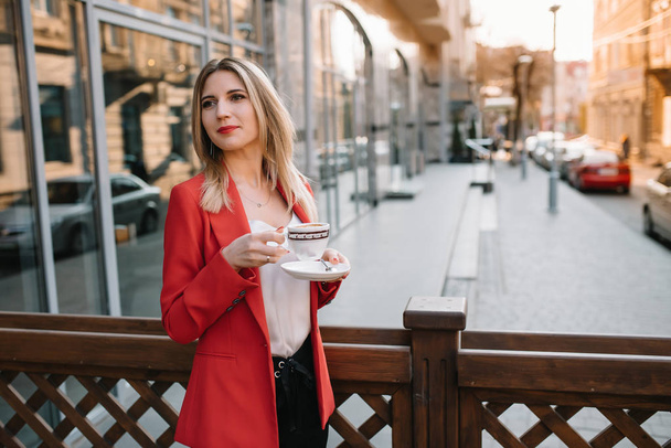 Beautiful young businesswoman with a disposable coffee cup, drinking coffee, and holding tablet in her hands against urban city background. - Φωτογραφία, εικόνα