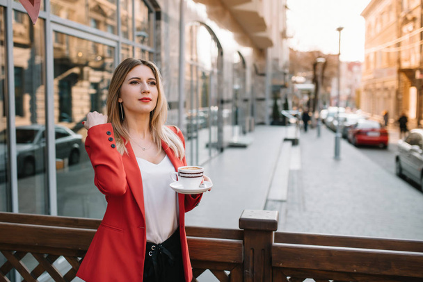 Beautiful young businesswoman with a disposable coffee cup, drinking coffee, and holding tablet in her hands against urban city background. - Foto, imagen