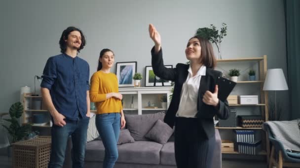 Realtor showing new house to couple talking while buyers looking around smiling - Video, Çekim