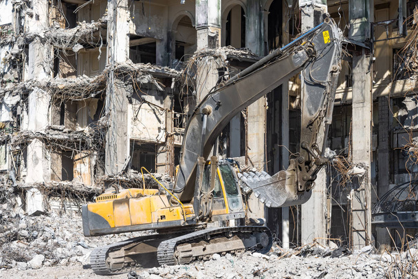 The ruins of a demolished collapsed building, piles of stones and dust. Excavator works with bucket. - Photo, Image