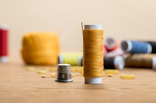 enfoque selectivo de la bobina de hilo con dedal en mesa de madera aislada en beige
 - Foto, Imagen
