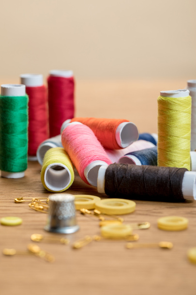 selective focus of colorful thread coils, safety pins and buttons isolated on beige - Photo, Image