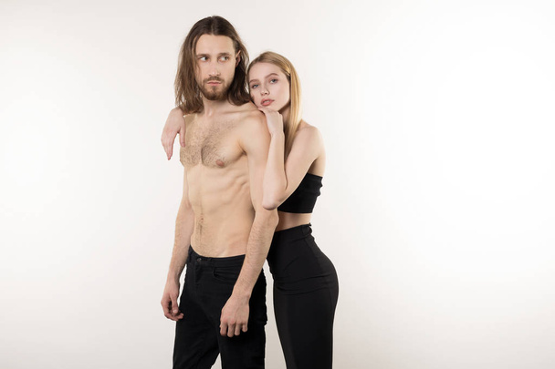 Young couple, bearded man with long hair and naked torso and beautiful girl with natural makeup hugging while posing in the studio - Photo, Image