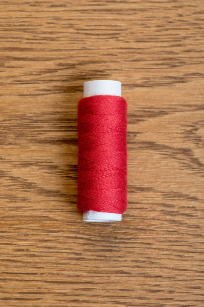 верхний вид катушки из красной хлопковой нити на деревянную поверхность
 - Фото, изображение