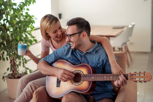 bel homme jouer de la guitare à sa petite amie dans leur maison
. - Photo, image