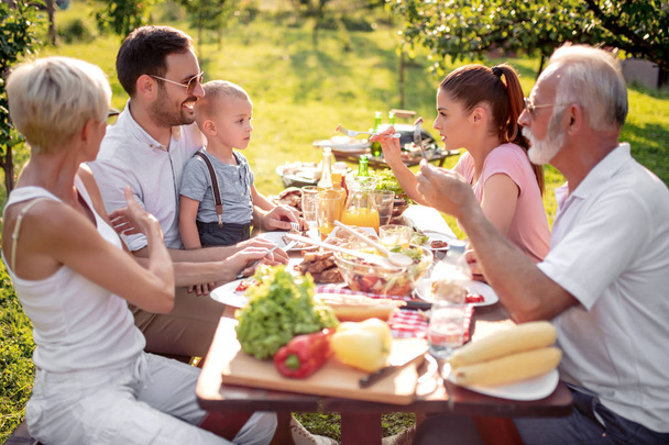 晴れた日に庭でピクニックをする家族の3世代. - 写真・画像