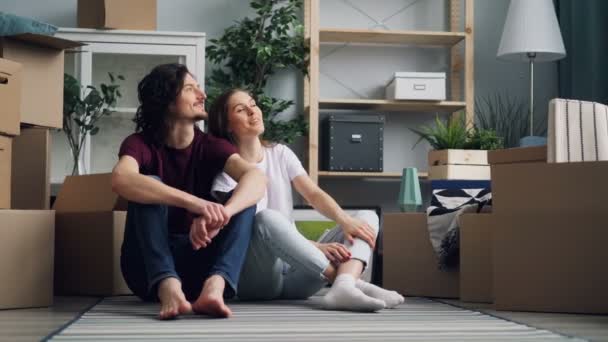 Šťastný pár mluví s úsměvem o novém bytě na podlaze s krabicí - Záběry, video