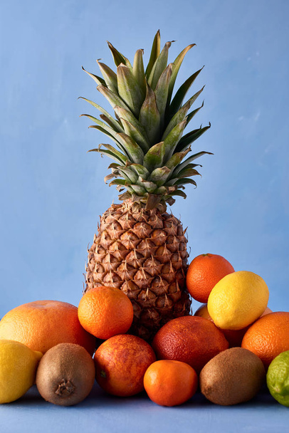 Vers fruit op een blauwe achtergrond. Smakelijke samenstelling van ananas, Mandarijn, kiwi, Siciliaanse sinaasappel, citroen, limoen en dranken. Exotische drinken fotografie met kopieerruimte. - Foto, afbeelding