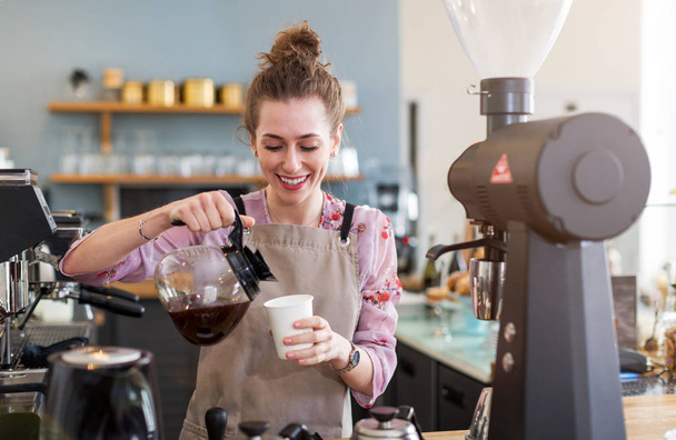 Young barista preparing coffee for customers at her cafe counter - Photo, Image